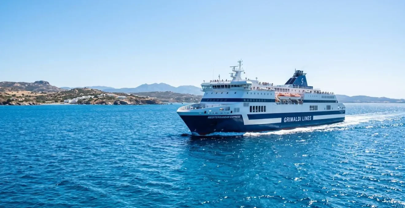 Un ferry moderne naviguant sur la mer Méditerranée sous un ciel bleu éclatant, vu depuis le pont supérieur avec une ambiance estivale lumineuse