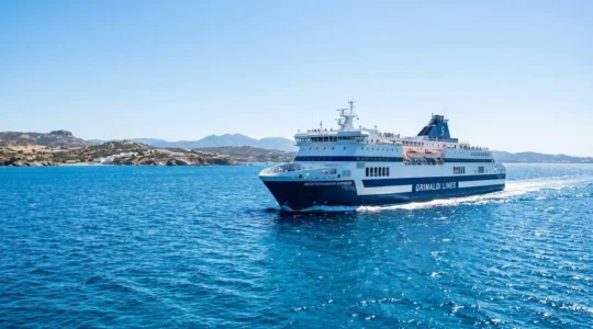 Un ferry moderne naviguant sur la mer Méditerranée sous un ciel bleu éclatant, vu depuis le pont supérieur avec une ambiance estivale lumineuse
