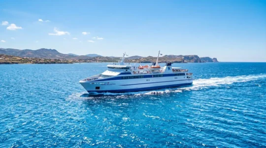 Un ferry moderne naviguant sur la mer Méditerranée sous un ciel bleu éclatant, vu depuis le pont supérieur avec une ambiance estivale lumineuse